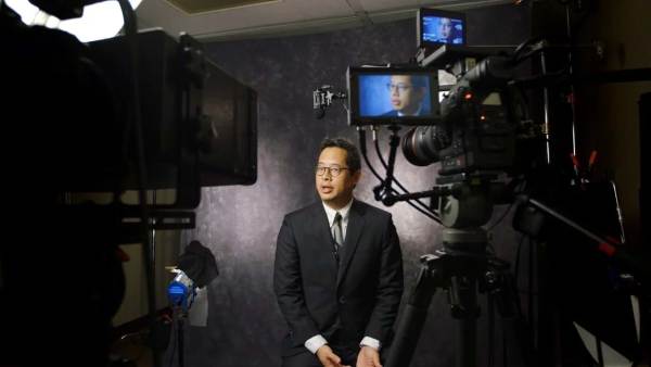 Jeff Chang sitting on a film set in front of multiple cameras with his face displayed on all monitors.
