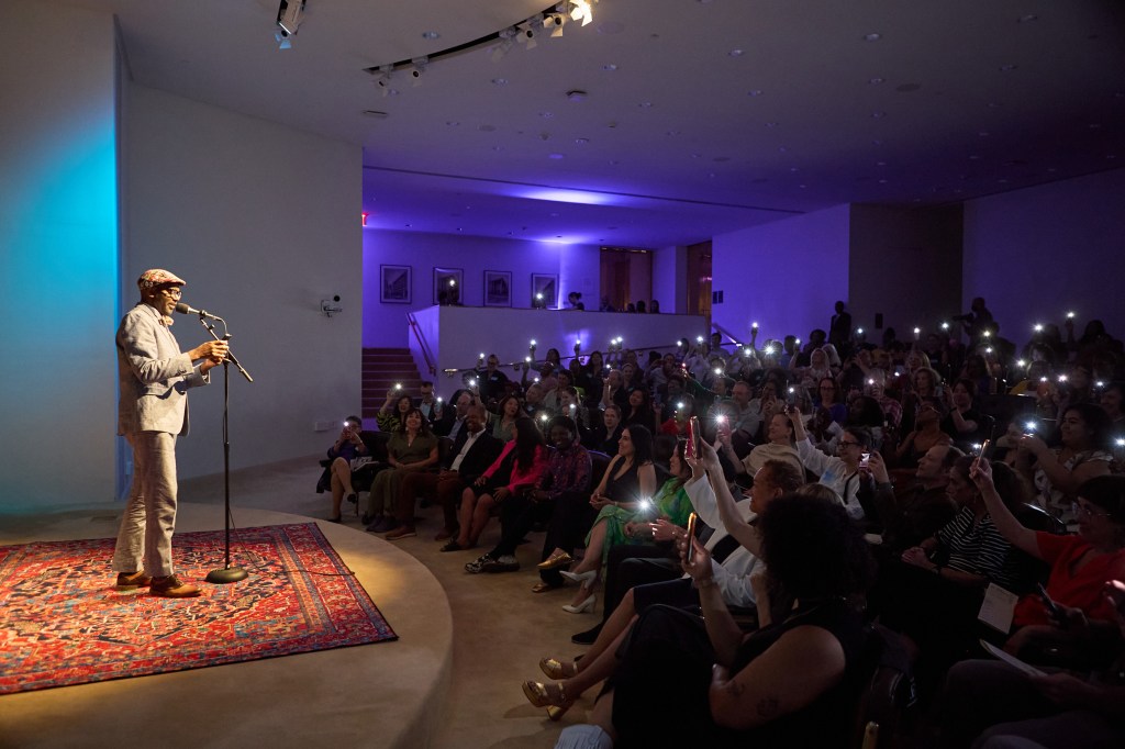 Host Jon Goode and the audience at the Ford Foundation auditorium. Audiences are holding up their phone lights to Jon who is on stage.