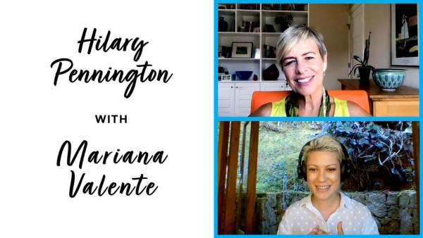 Hilary Pennington has short hair with blond highlights and is wearing a yellow top with green scarf and sitting on an orange chair. Mariana Valente has a short bleached blond hair, is wearing a white polkadot top and standing outside in front of a stone wall with bushes in the background..