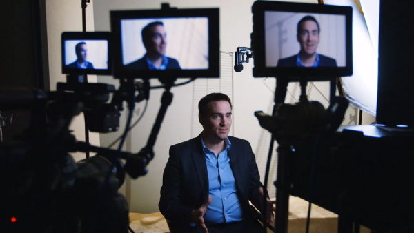 Michael Clemens sitting on a film set in front of multiple cameras with his face displayed on all monitors.